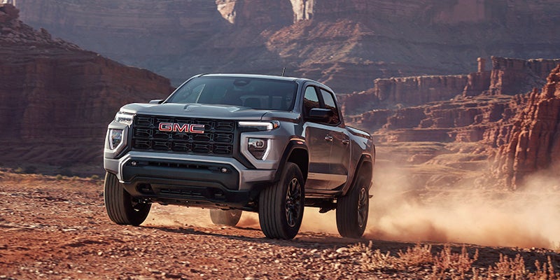 A GMC Sierra driving through a vast desert landscape under a clear blue sky.