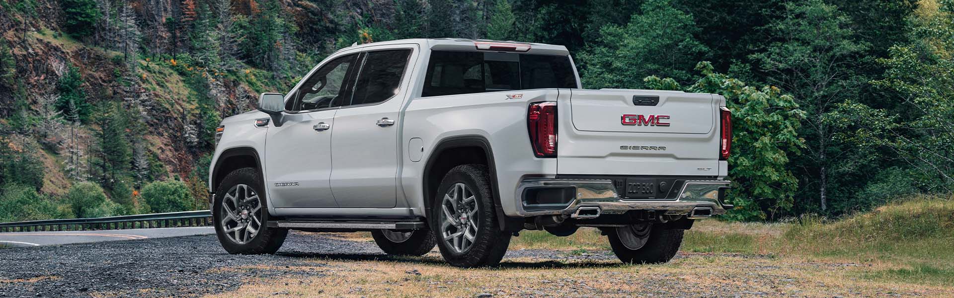 White GMC Sierra pickup truck parked near a forest road.