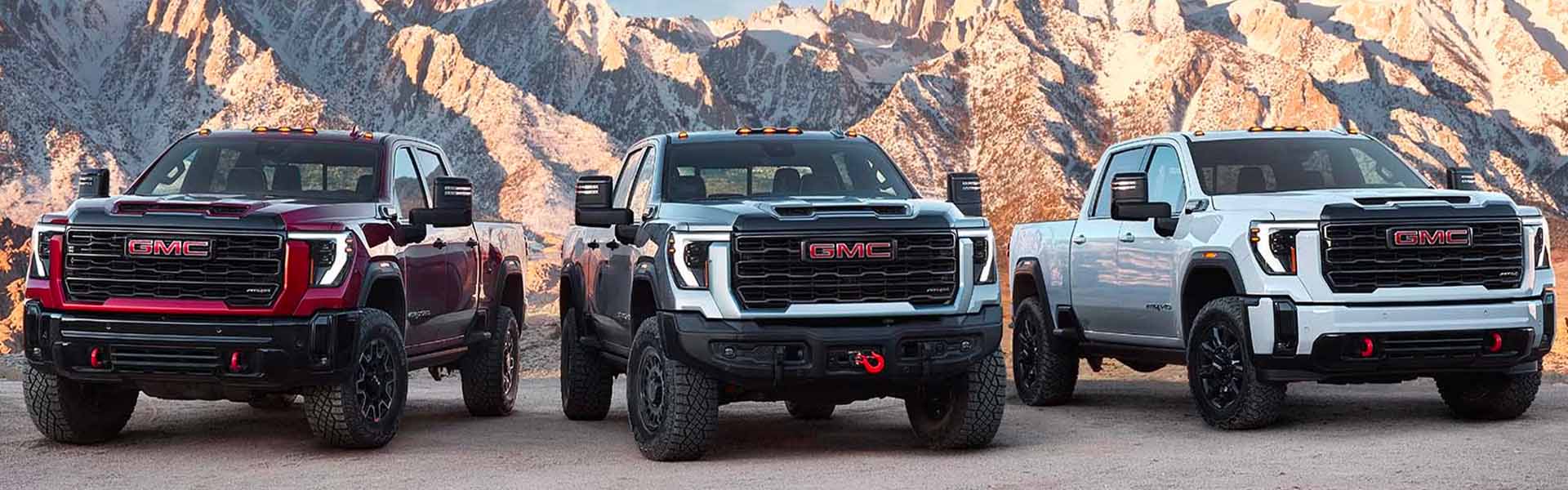 Three GMC heavy-duty trucks with mountain backdrop.