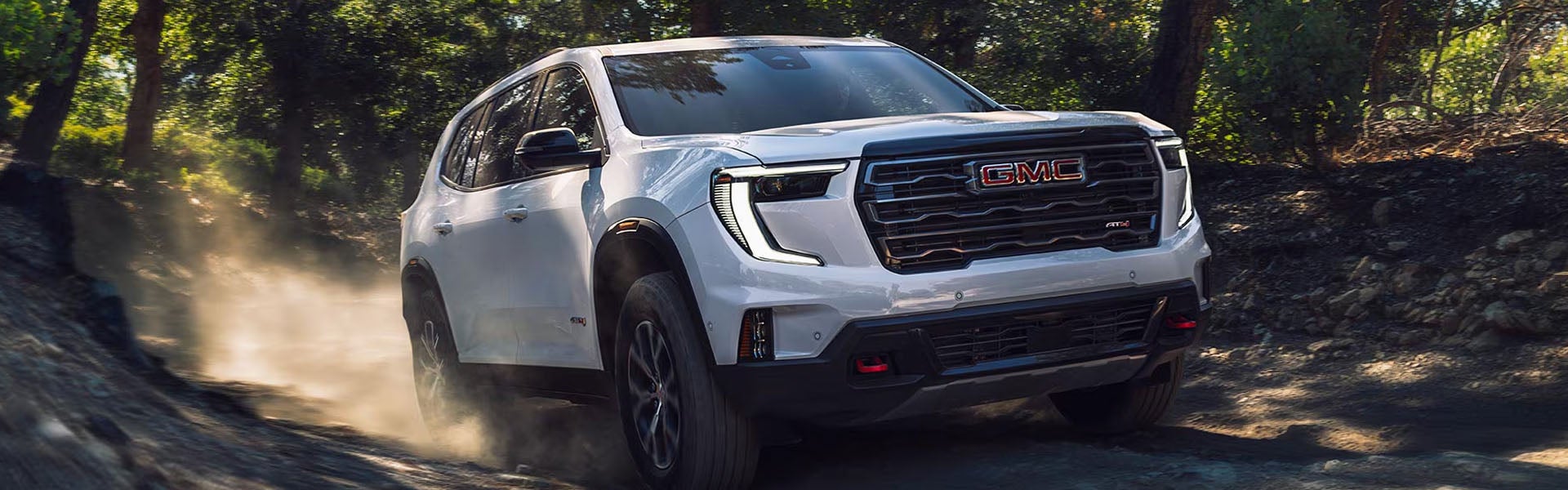 White GMC SUV driving off-road through a wooded trail.