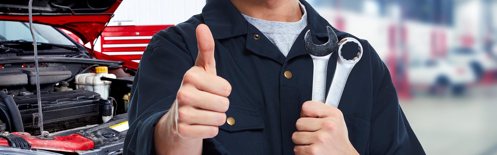 Auto mechanic giving a thumbs-up beside an open car hood.
