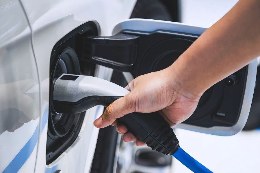 A person holds an electric car charging cord, preparing to charge an electric vehicle at a charging station.